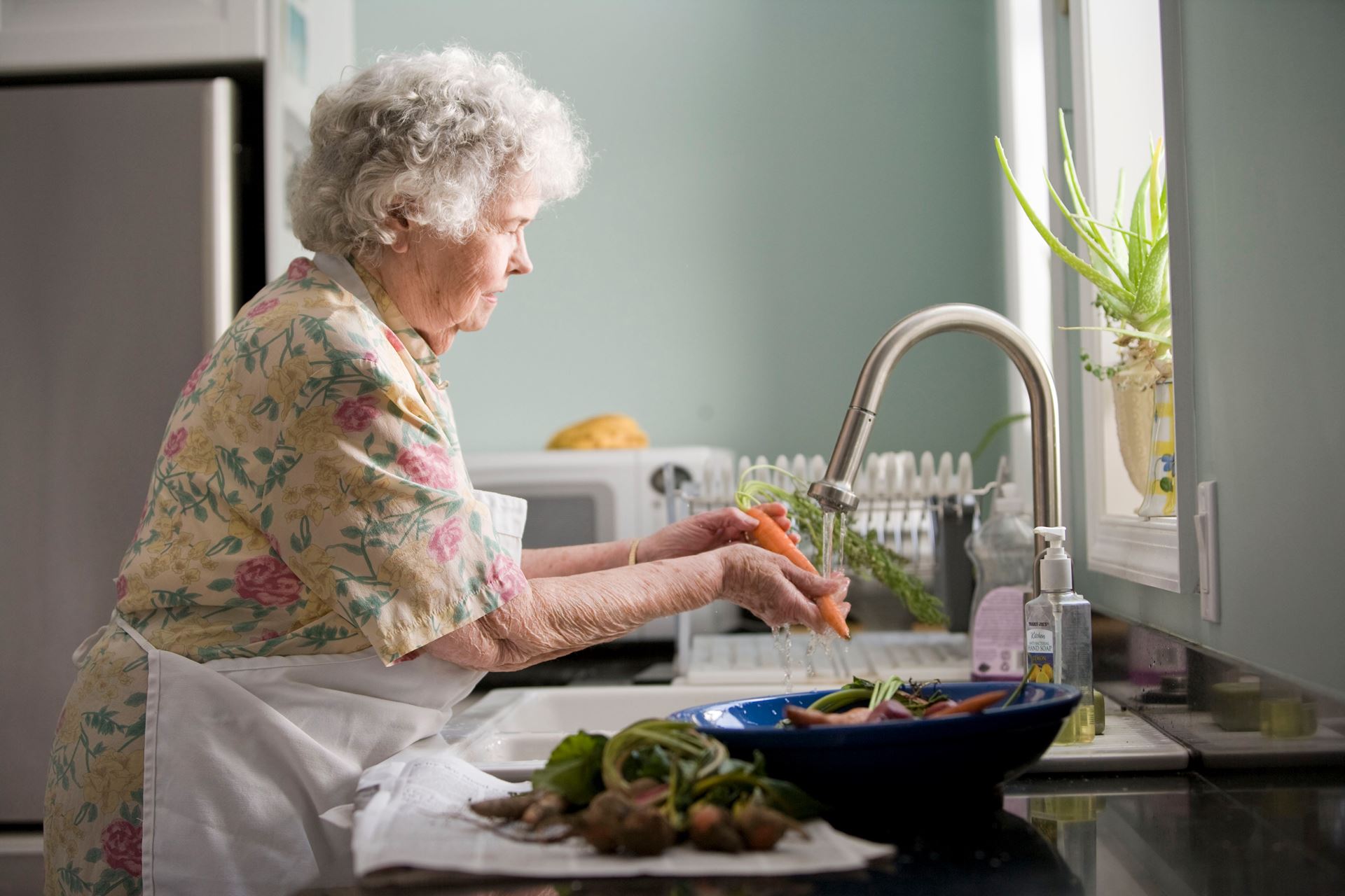 An elderly woman washing vegetables at a sink