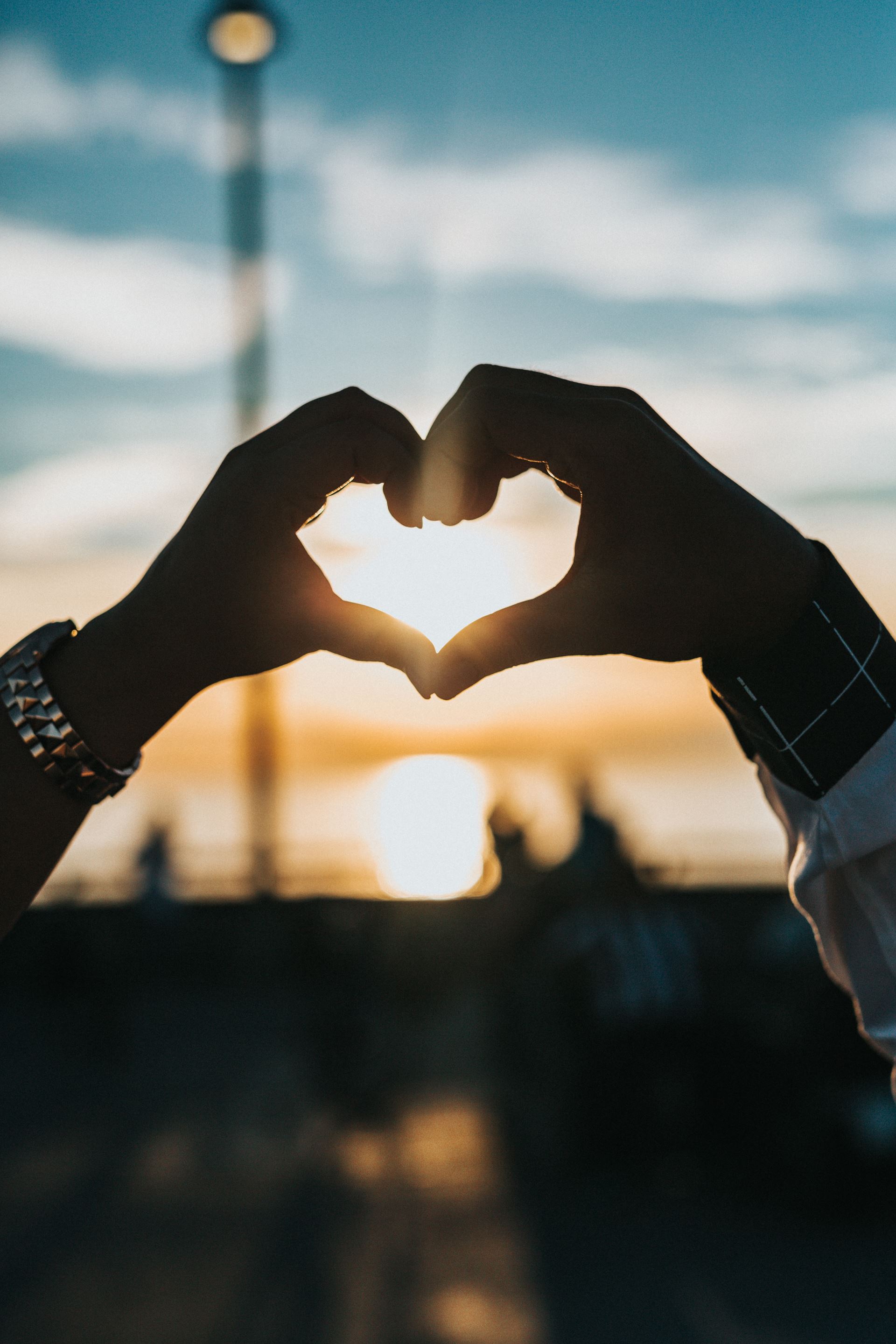 a person making a heart shape with their hands, a sunset in the background