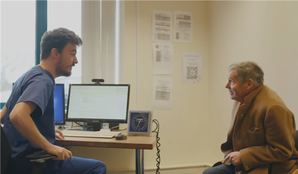 A healthcare assistant speaking to an older man in a GP surgery office