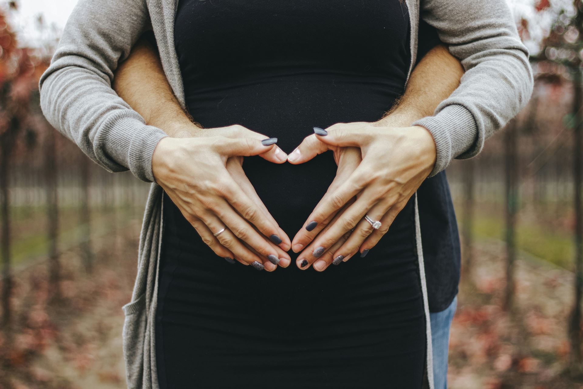 a pregnant woman and a man stood behind her - they both have their hands on her baby bump