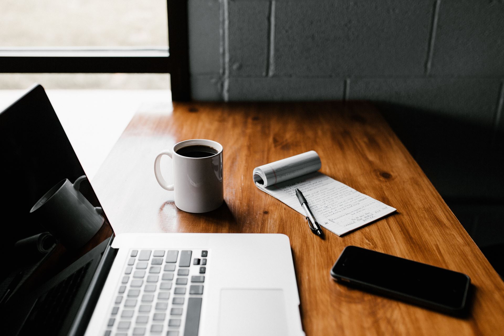 a laptop on a table, a coffee cup and a note pad