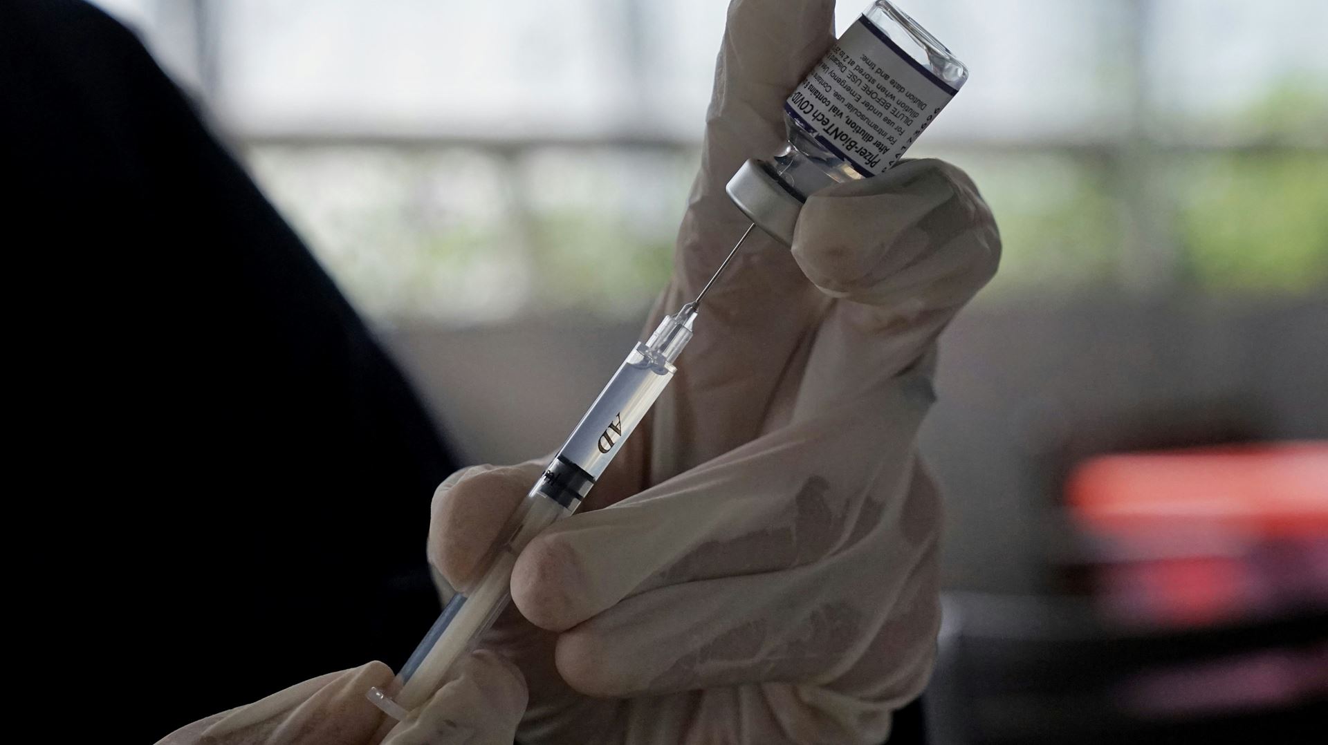 a clincian using a syringe to draw a vaccine from a vial